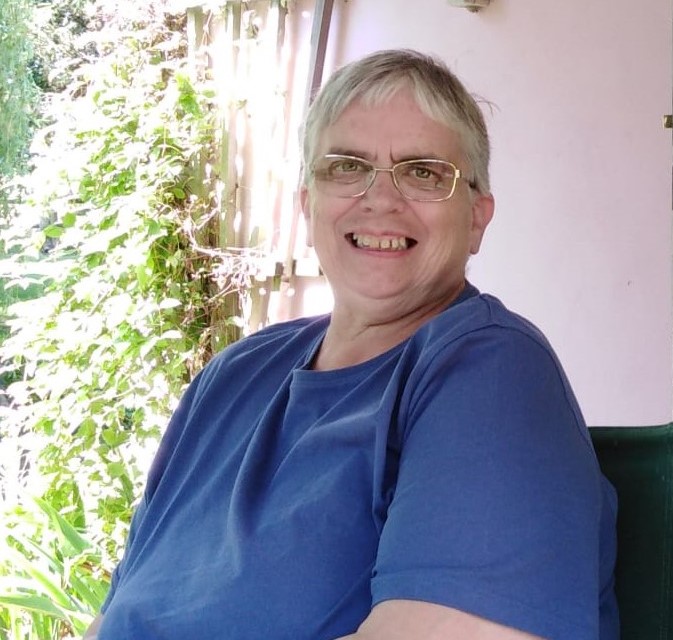 alt=“a happy person in a blue t shirt wearing glasses sitting by a sunlit window at a thriving garden