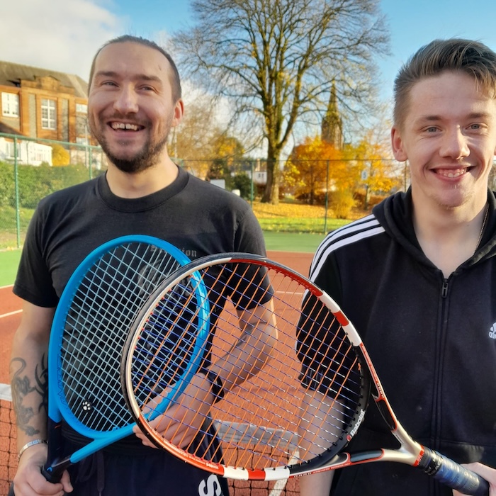 two happy men standing beside each other outside with tennis raquets