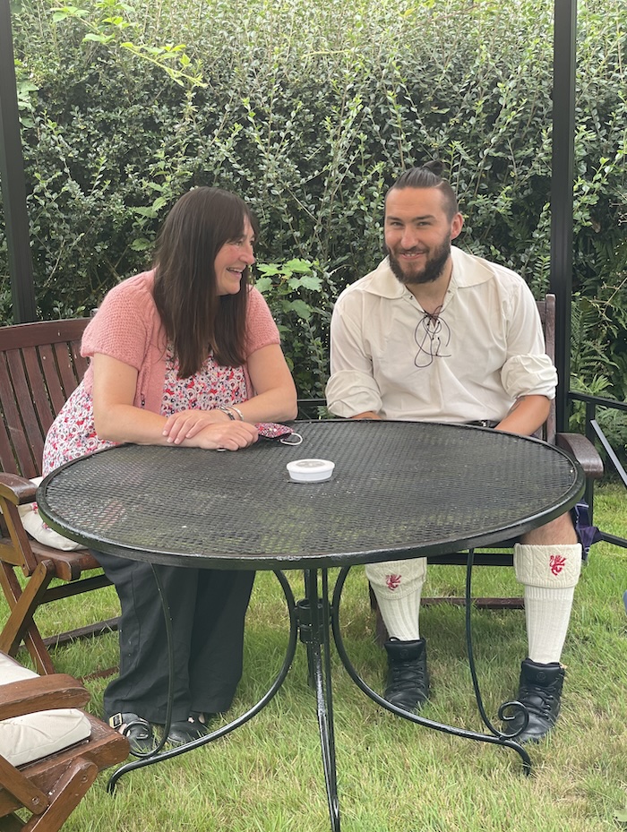 two people laughing and chatting at a table in a plush garden