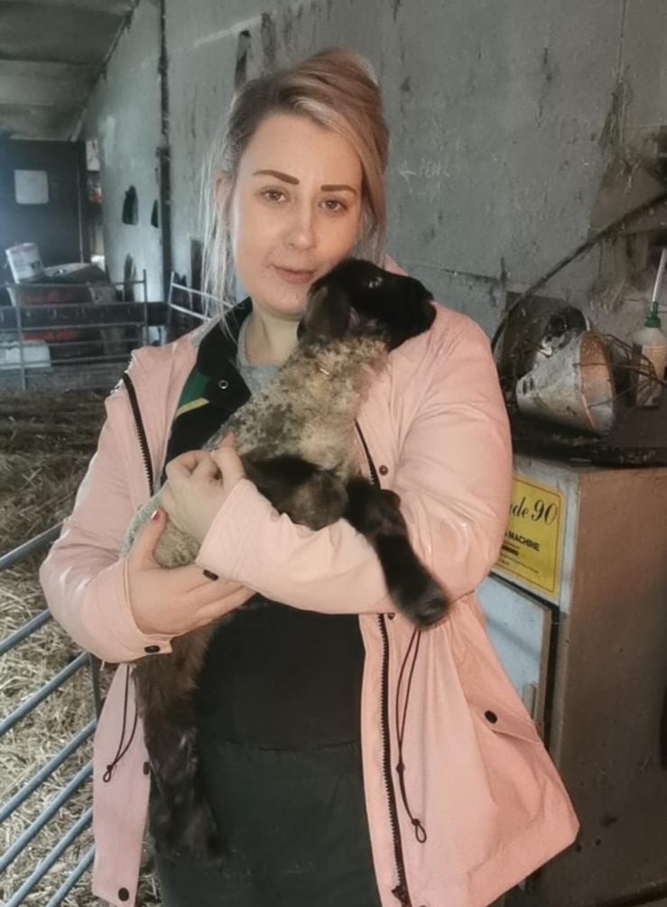 person cradling a lamb while standing in a farming building 