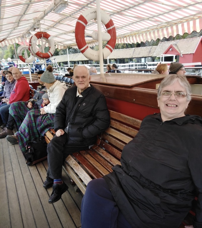 a-row-of-people-sitting-on-a-wooden-bench-taking-a-trip-on-a-wide-decked-tourist-boat